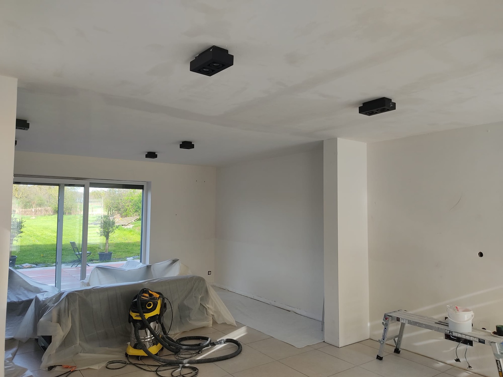 Pièce de vie en préparation : plafond et murs lissés, sols bâchés, ponceuse reliée à l'aspirateur